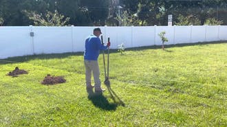 A man digging a hole in the yard for a fence pole.